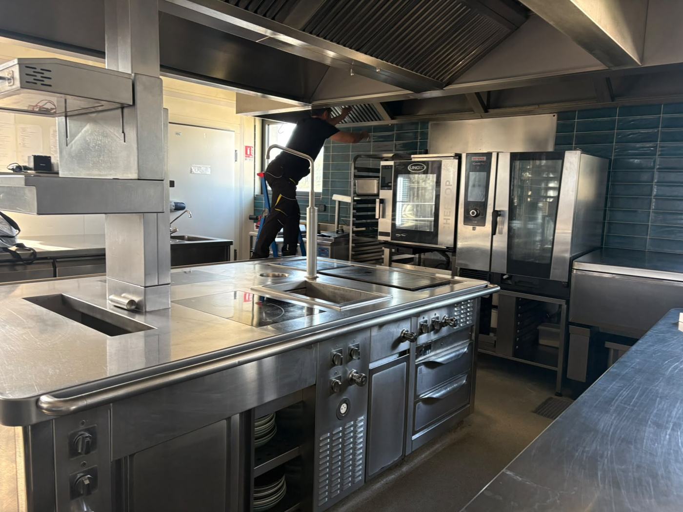 Technicien KAIROS nettoyant la hotte d'une cuisine professionnelle équipée de fours mixtes