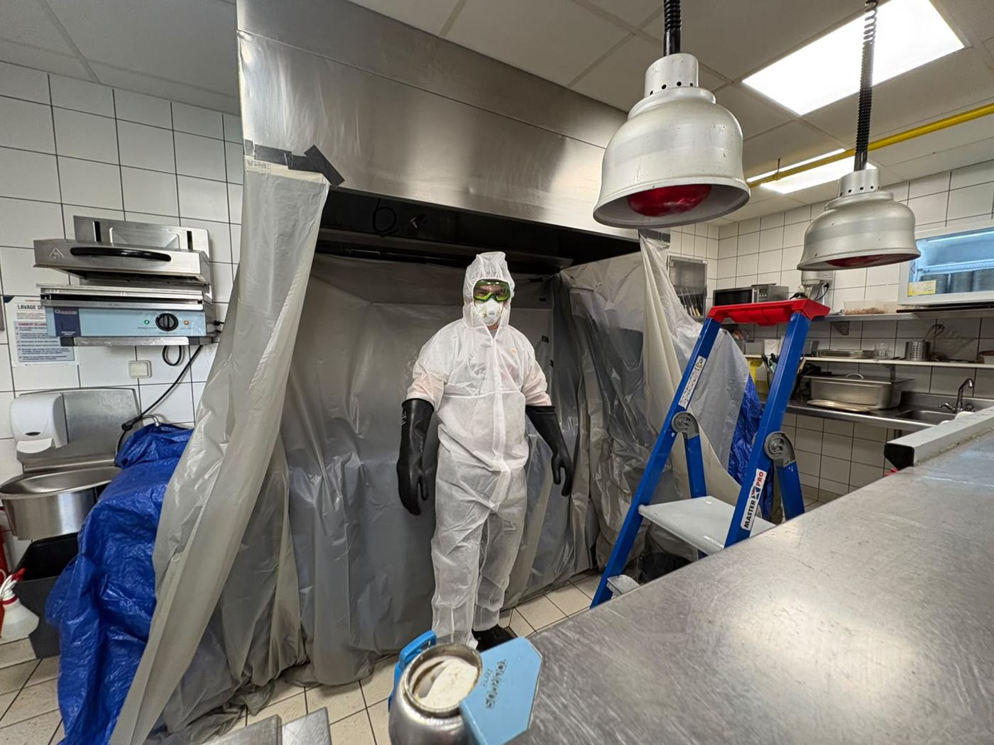 Technicien en combinaison devant une hotte bâchée pour le dégraissage
